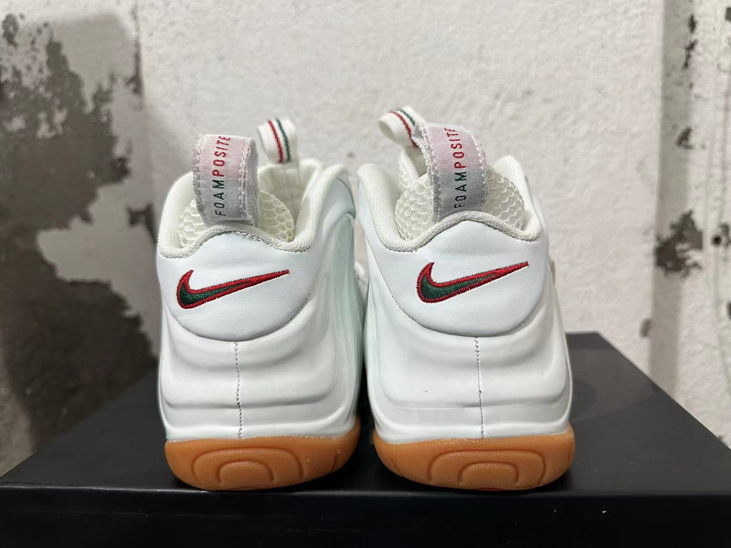 Rear view of white Nike Foamposite sneakers with red-and-green heel Swooshes and gum-colored outsoles
