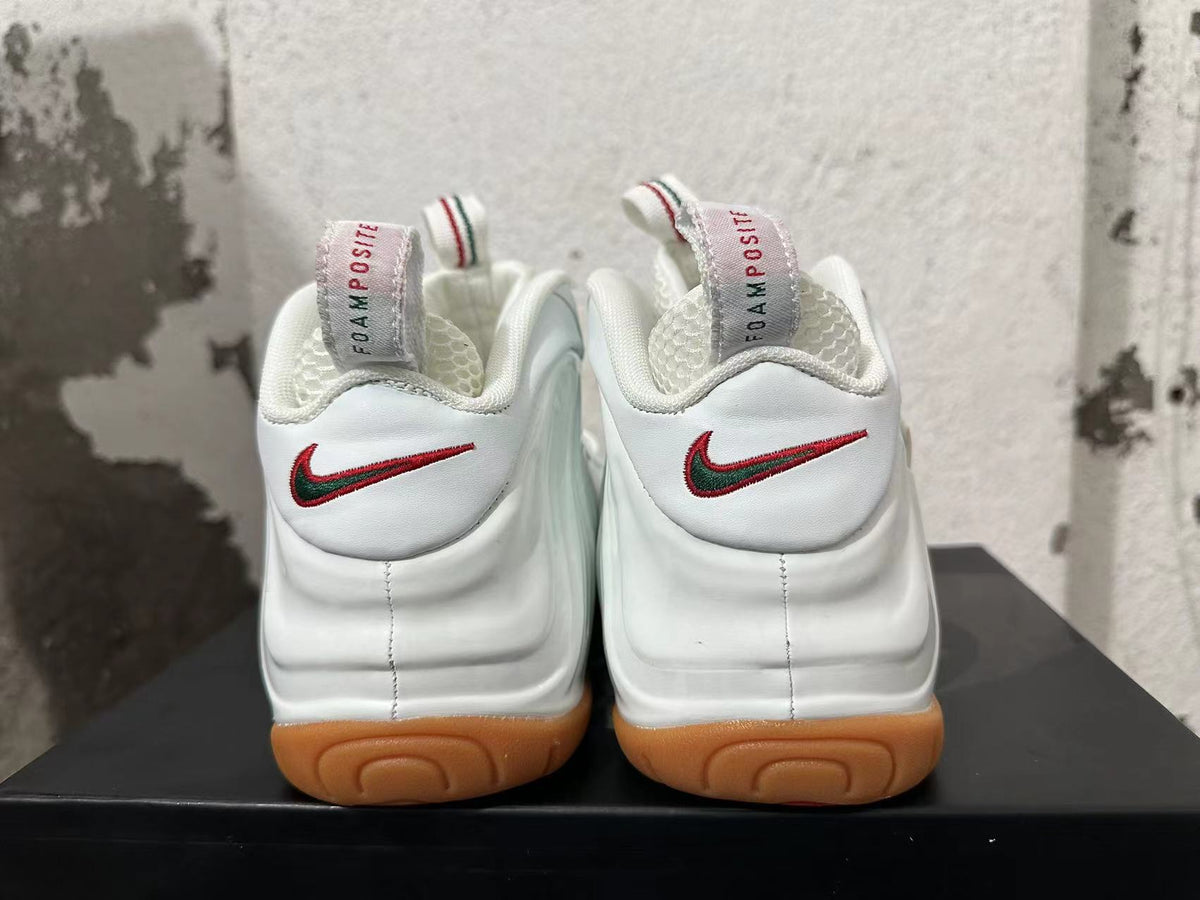 Rear view of white Nike Foamposite sneakers with red-and-green heel Swooshes and gum-colored outsoles