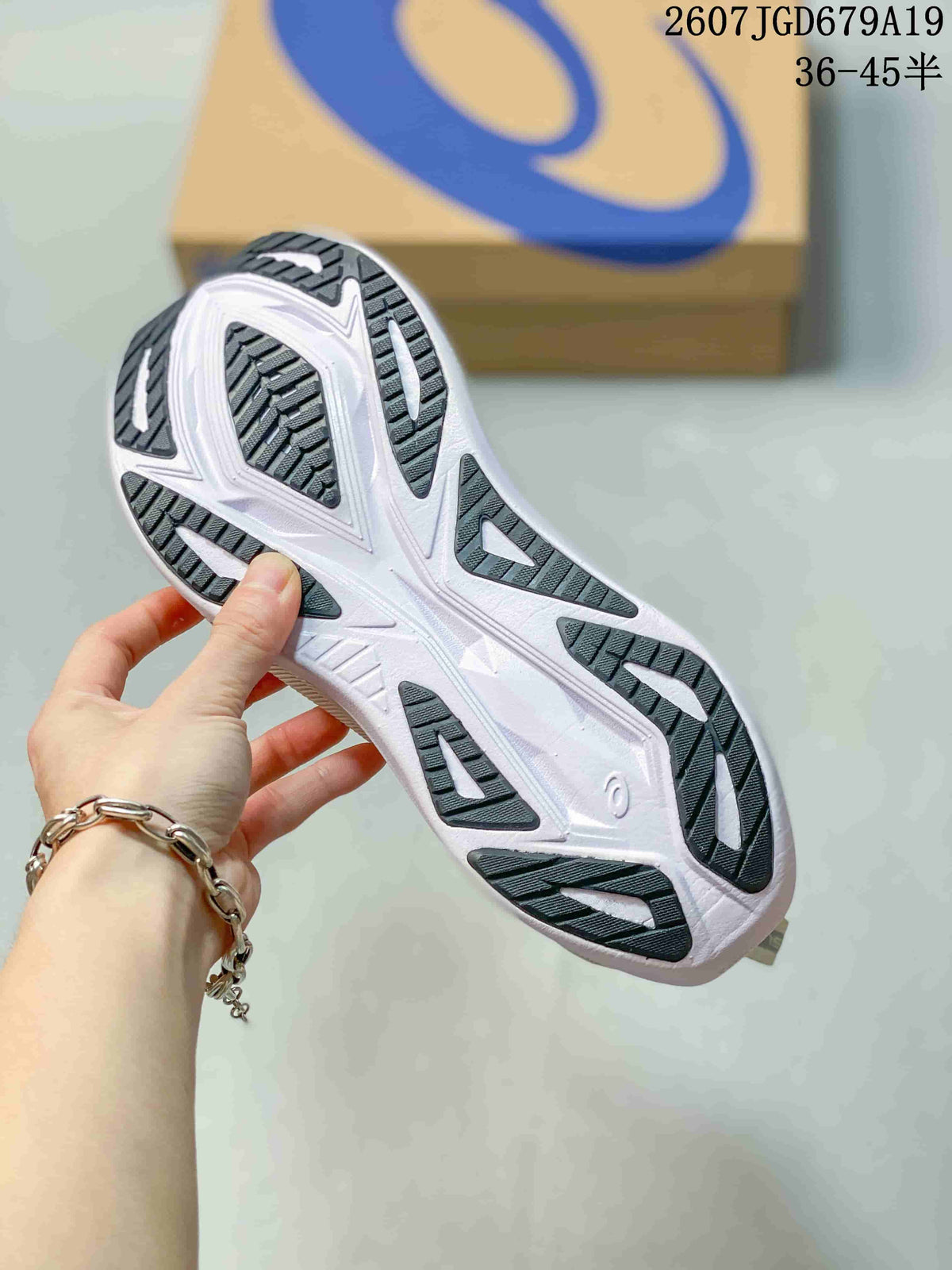 Close-up of the patterned outsole on a white ASICS running sneaker, showing dark traction sections and white structural details.