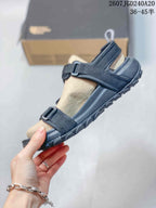 Side view of the black sandal showing the tan footbed, adjustable straps, buckle, and raised outsole.