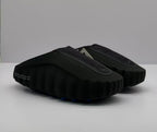 Three-quarter view of a pair of black slide sandals with textured uppers and circular emblems.
