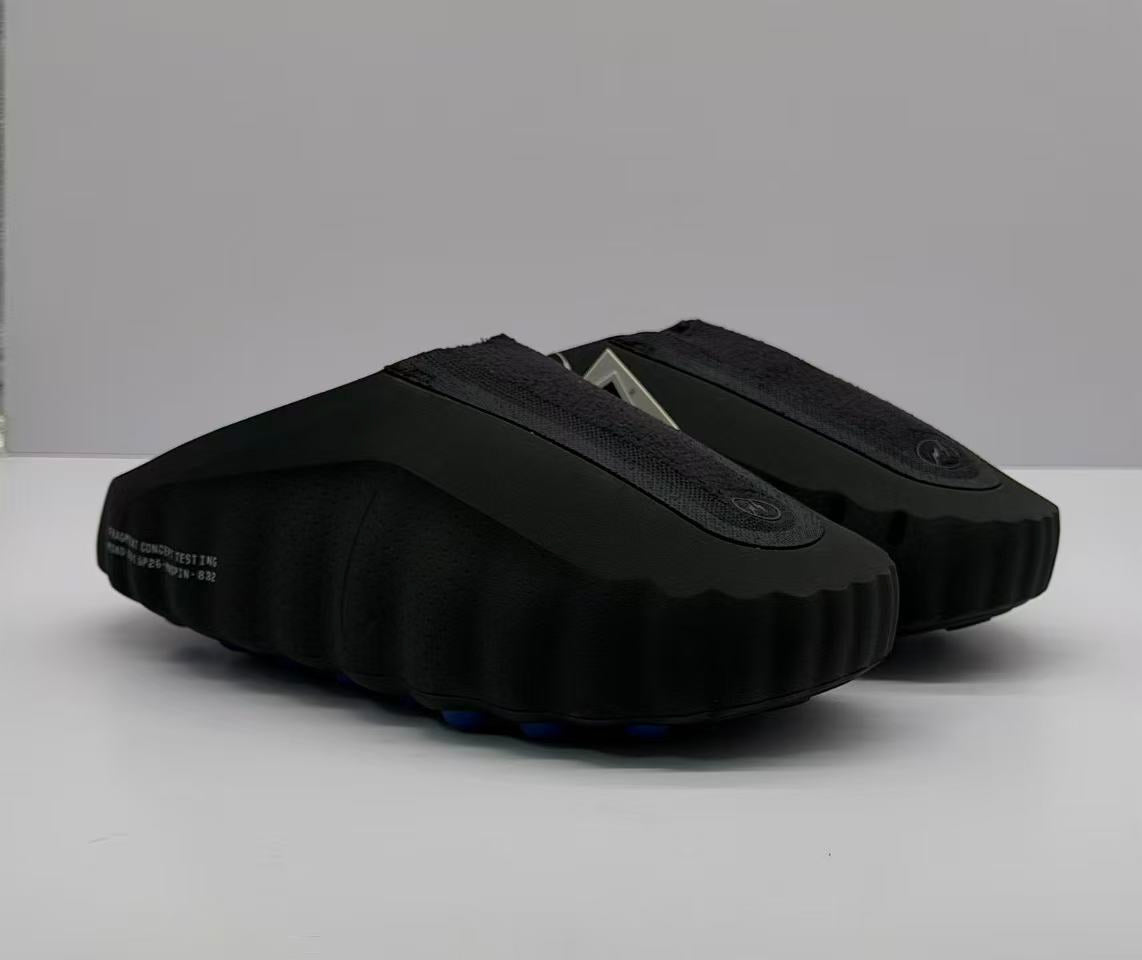 Three-quarter view of a pair of black slide sandals with textured uppers and circular emblems.