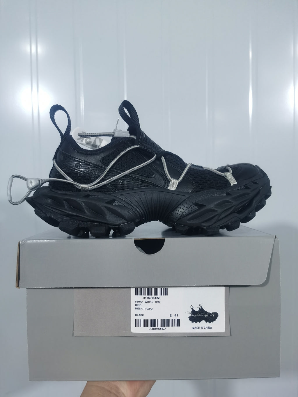 Black Nike sneaker displayed on a shoebox, showing the mesh upper, cord detailing, rugged outsole, and box label.