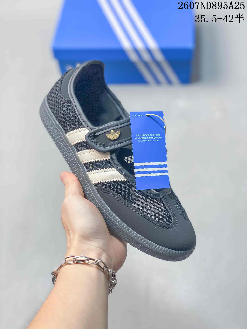 Angled side view showing the black upper, light three-stripe detailing, Mary Jane strap, and product hangtag.