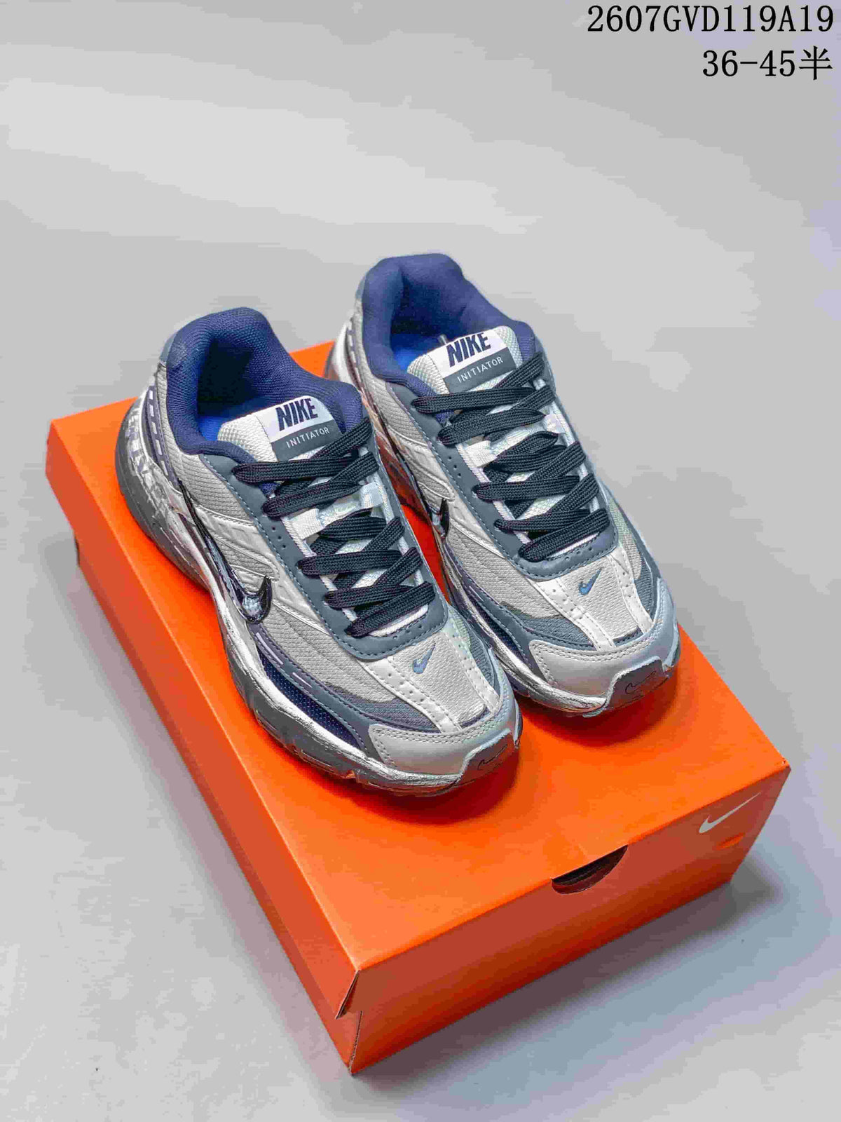 Pair of black, grey and white Nike Initiator sneakers displayed on an orange shoebox.