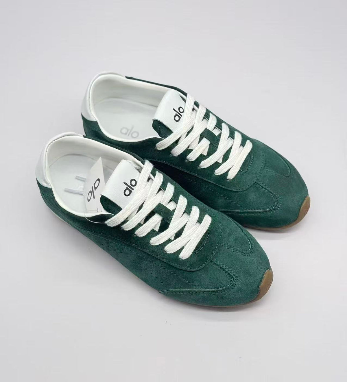 Top three-quarter view of green Alo sneakers showing the lacing, stitched toe panels, and white interiors.