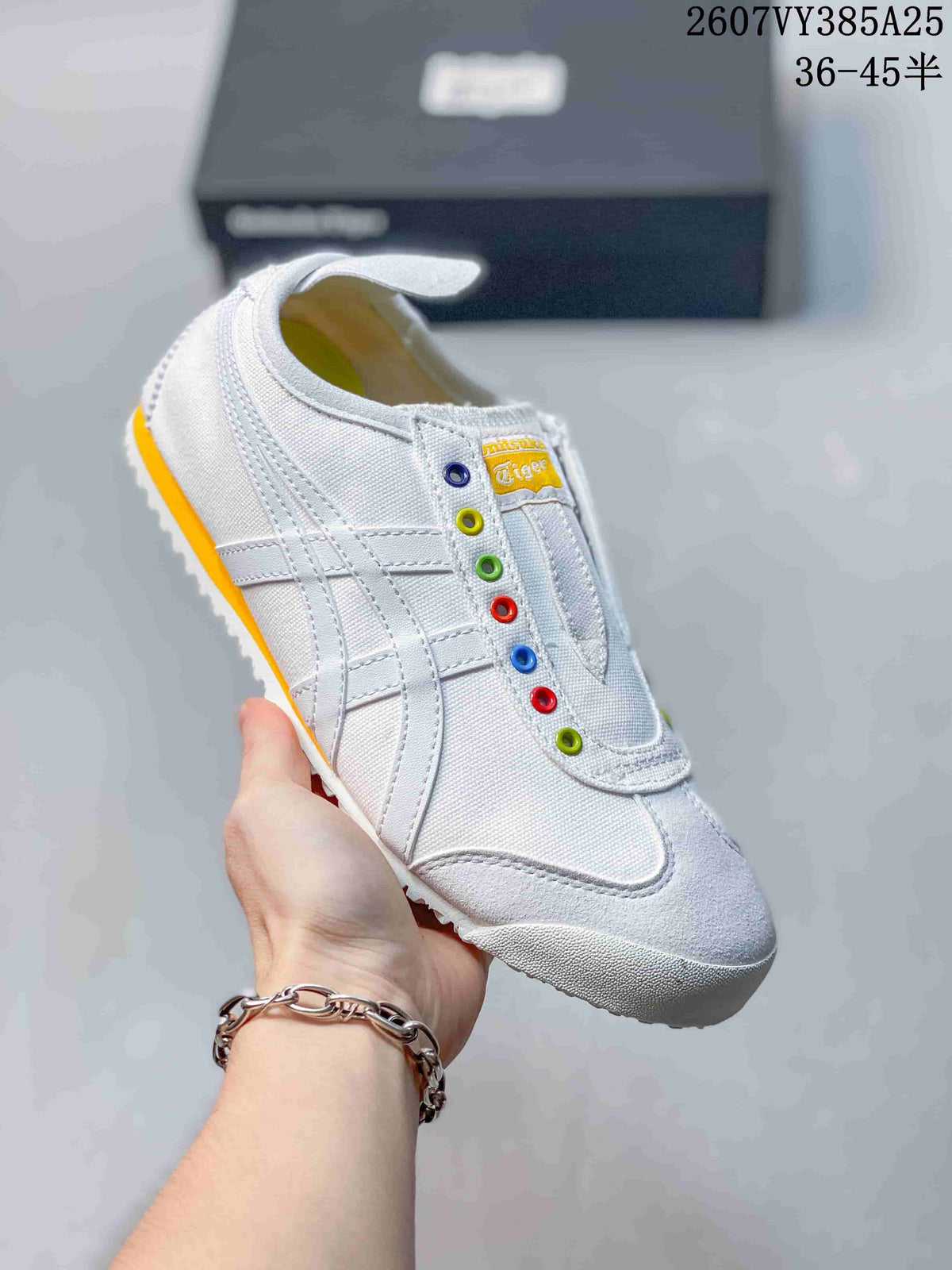 White slip-on sneaker with colorful eyelets, white side stripes and a yellow outsole accent.