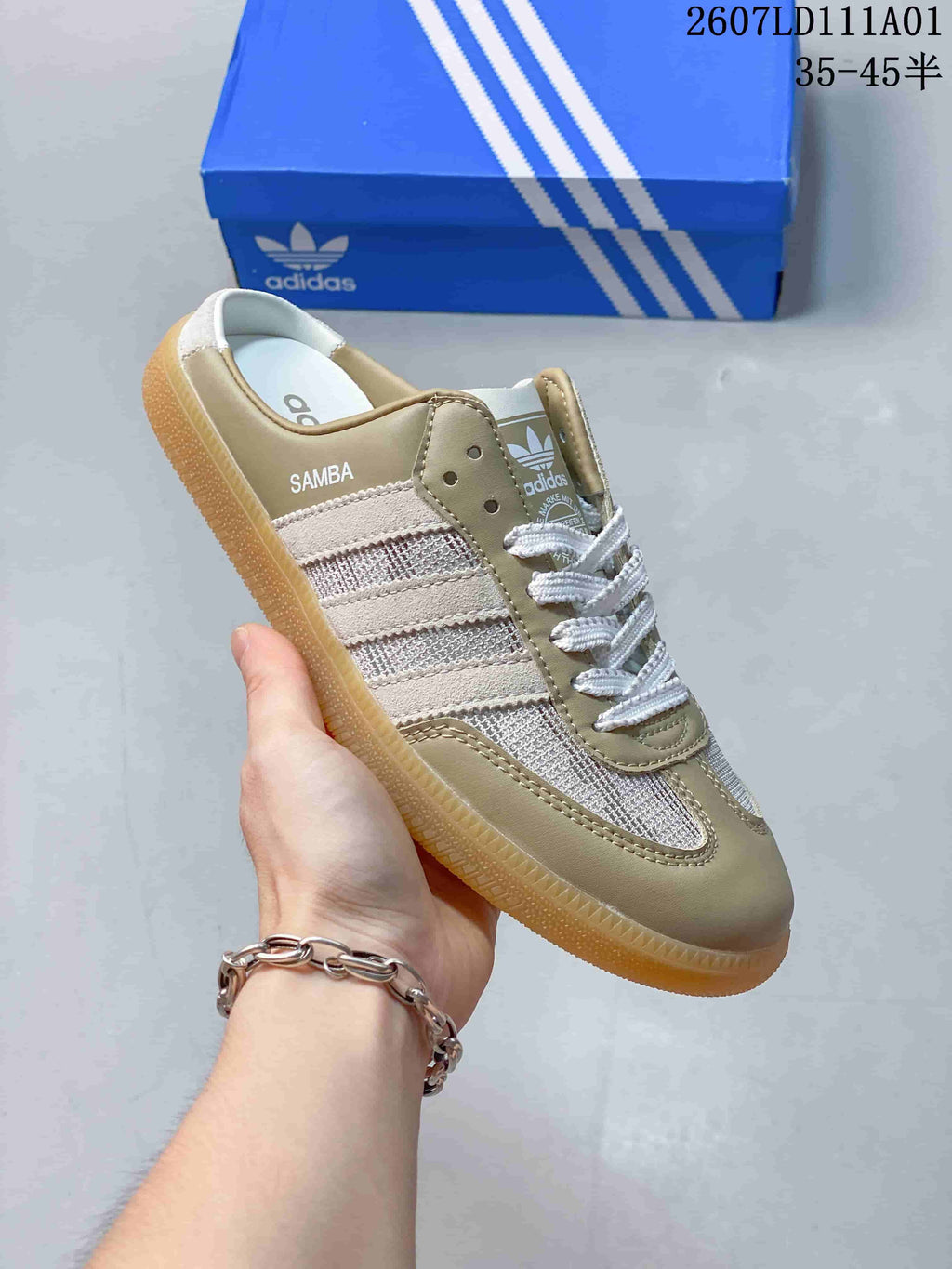 Taupe Adidas Samba-style mule sneaker with an open heel, white laces, striped side panels, and gum-colored outsole.