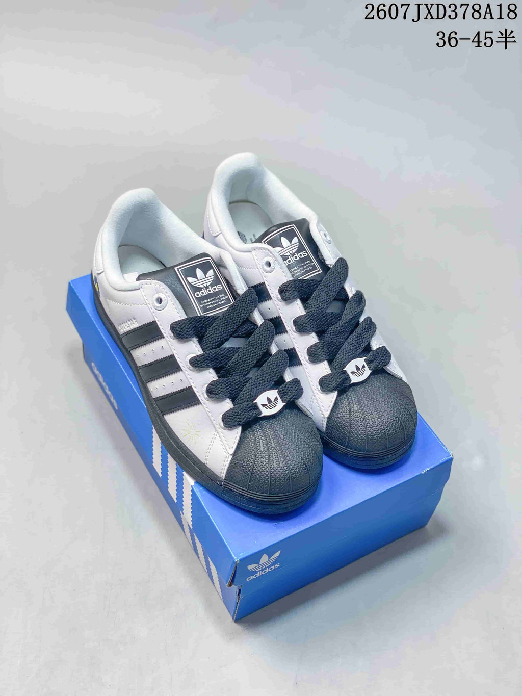 Pair of white and black adidas Originals Superstar sneakers displayed on a blue shoebox, showing the shell toes and dark laces.