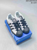 Pair of white and black adidas Originals Superstar sneakers displayed on a blue shoebox, showing the shell toes and dark laces.