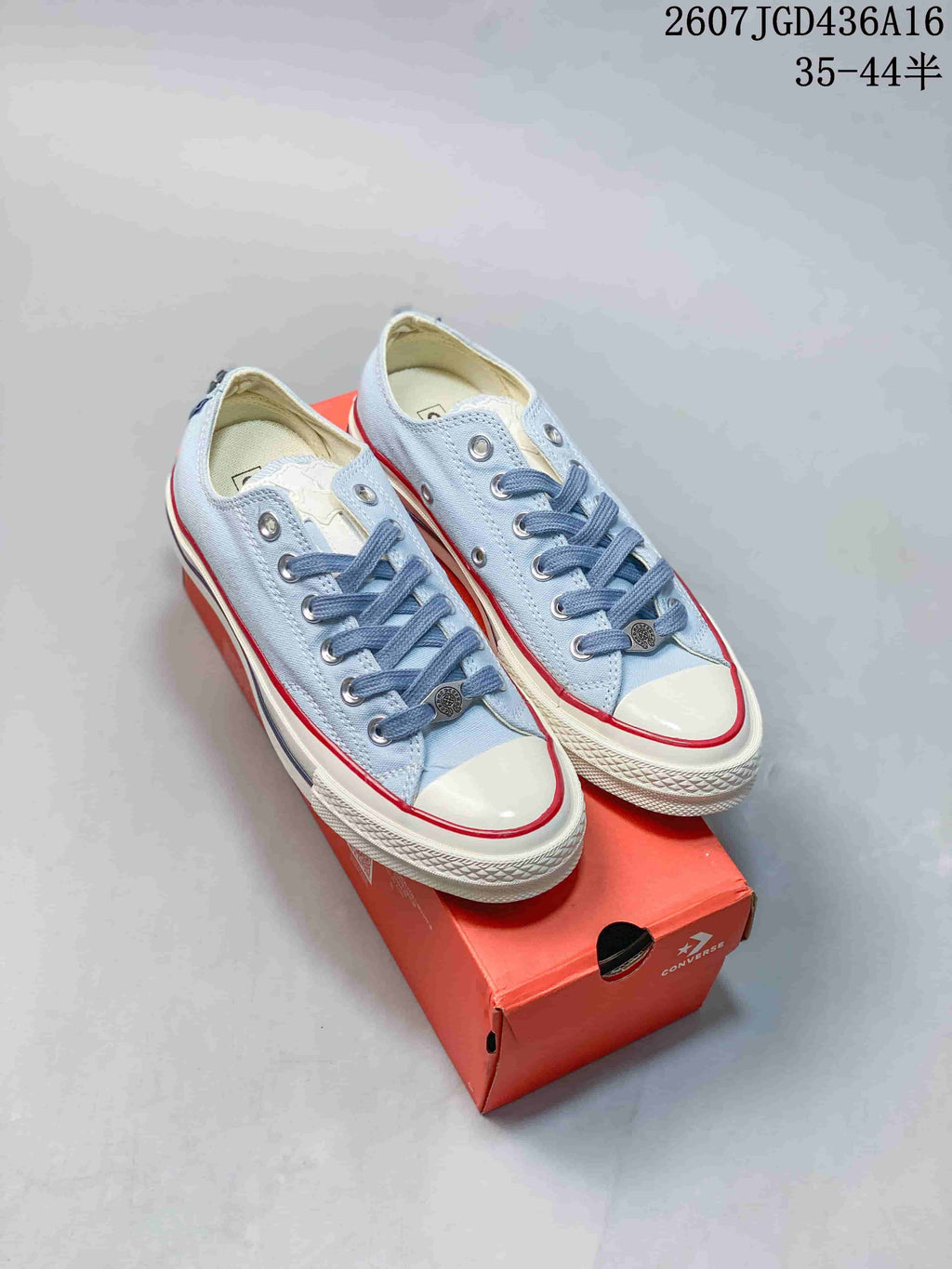 Pair of light blue Converse All Star low-top sneakers displayed on a red shoe box, showing blue laces, white toe caps, and red sole stripes.
