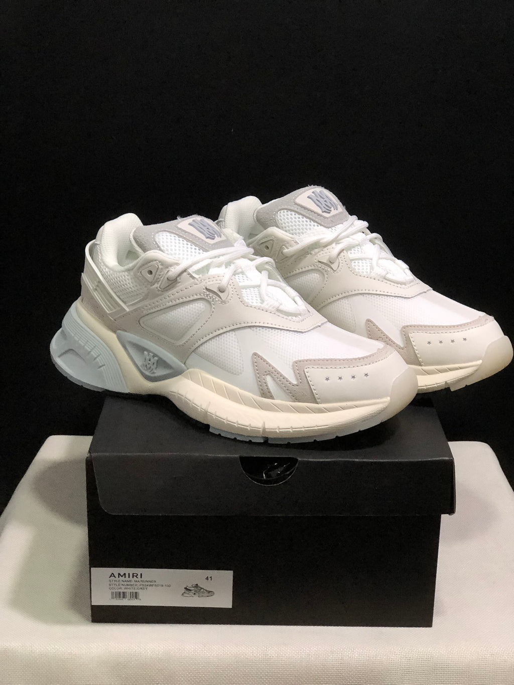 Pair of white and light grey AMIRI MA Runner sneakers displayed on a black shoebox labeled size 41.
