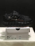 Side view of black Nike Mind 002 sneakers displayed on a shoebox, showing orange perforation accents and the box label.
