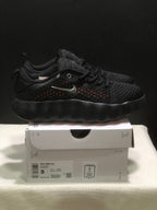 Side view of black Nike Mind 002 sneakers displayed on a shoebox, showing orange perforation accents and the box label.