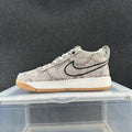 Low-top sneaker with a pale grey snake-print pattern, dark outlined side swoosh, white midsole, and gum-colored outsole