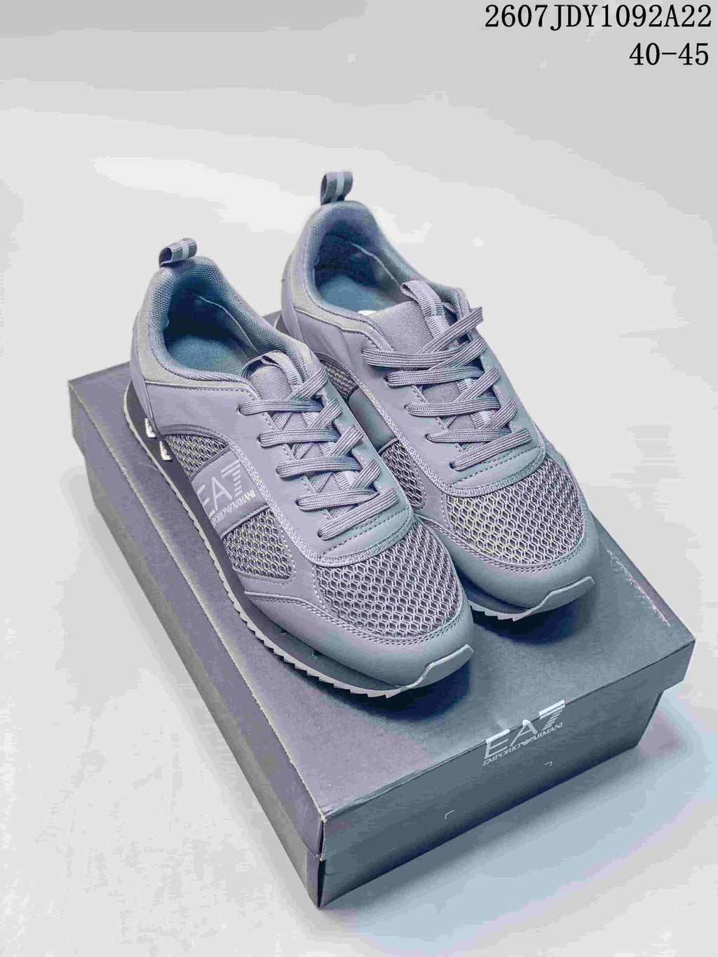 Pair of gray Emporio Armani EA7 low-top sneakers displayed on a branded shoe box, with the style code and EU size range visible above.
