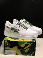 Pair of white BAPE STA low-top sneakers with green camouflage star panels and matching laces displayed on a camouflage shoebox.