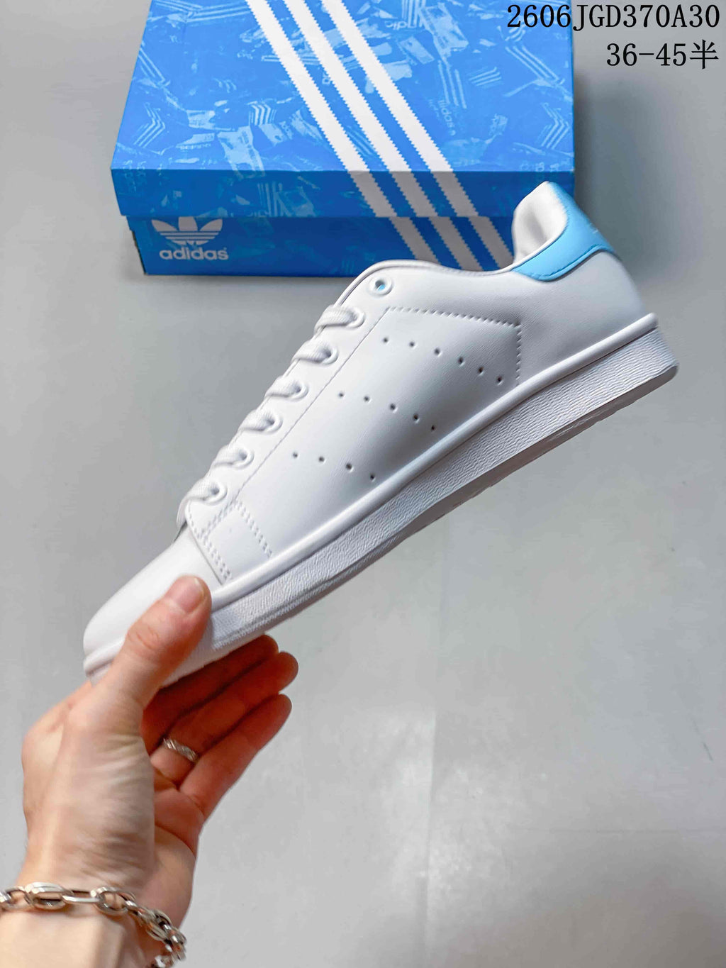 Side view of a white Adidas Stan Smith sneaker with perforated panels and a light-blue heel tab