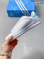 Side view of a white Adidas Stan Smith sneaker with perforated panels and a light-blue heel tab