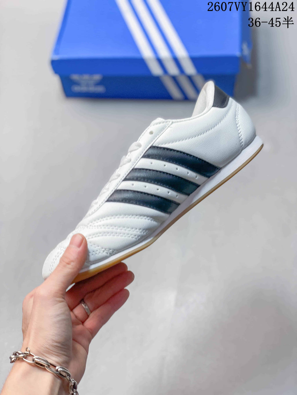 Side profile of the white adidas Taekwondo sneaker showing dark navy stripes, stitched panels, low-top collar, and gum-colored outsole.