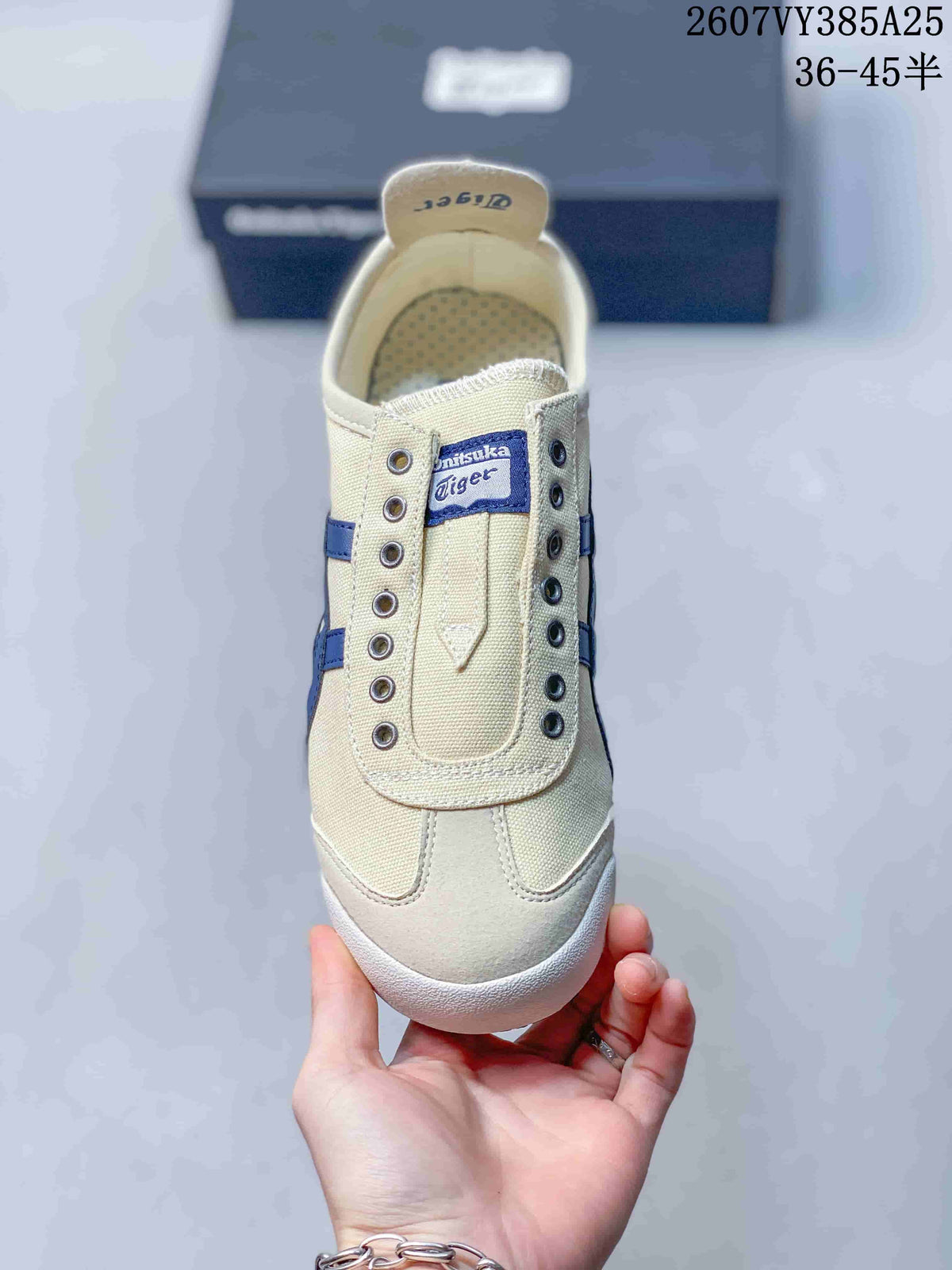 Front view of the cream slip-on sneaker showing the blue Onitsuka Tiger tongue label, eyelets, and rounded toe.