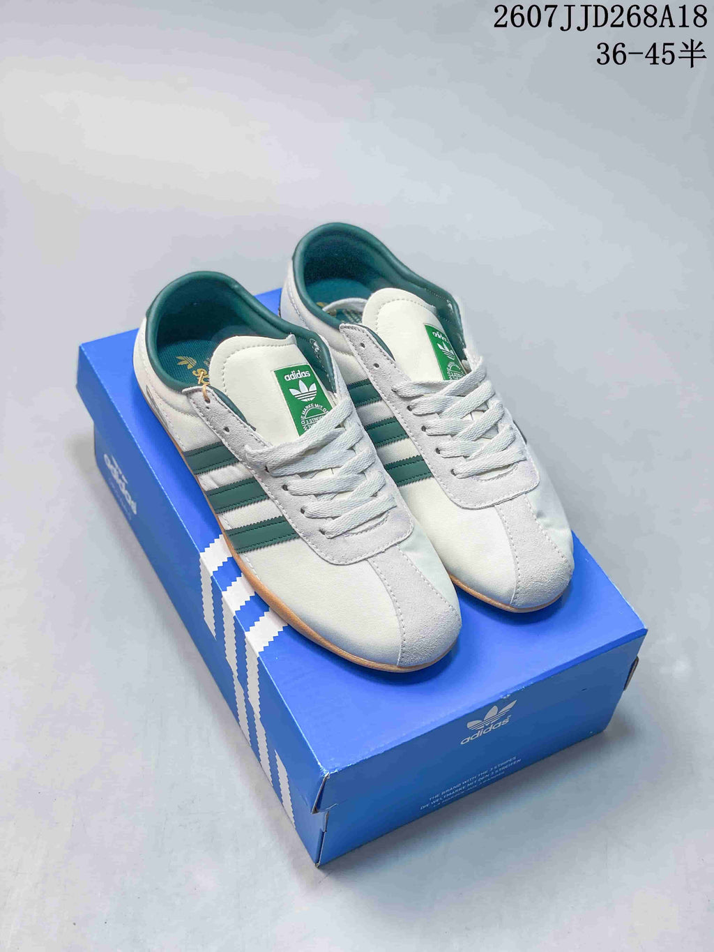 White adidas Originals Tokyo low-top sneakers with green stripes displayed on a blue adidas shoe box; overlay text shows style 2607JJD268A18 and size range 36–45.5.