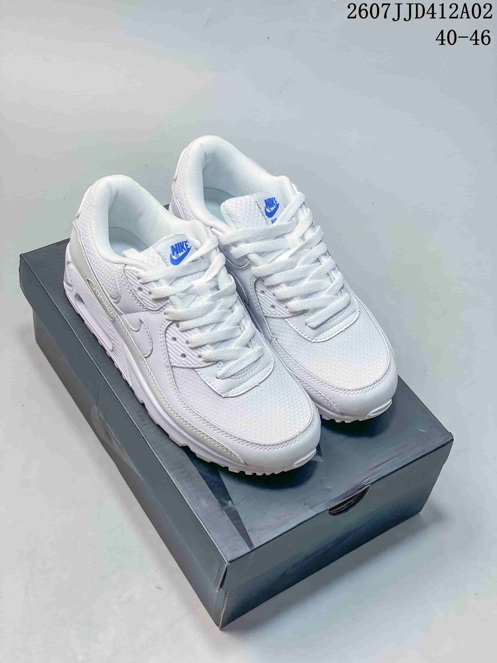 Pair of white Nike Air Max 90 sneakers with blue accents on a dark shoebox