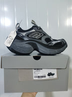 Side view of a black and grey Skechers sneaker resting on its box; the box label shows size E 40 and color BLACK/GREY.