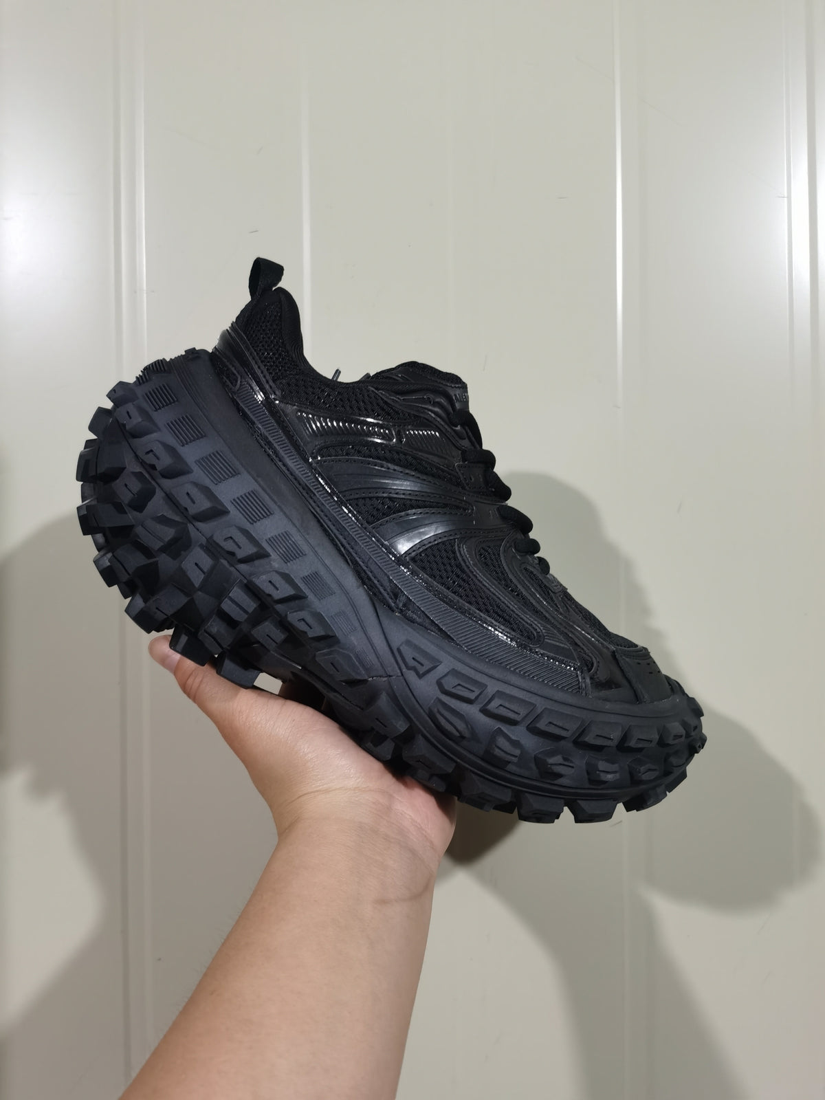 Black chunky sneaker held in hand, showing its layered side panels and heavily lugged outsole.