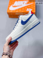 Side profile showing the white low-top sneaker, blue Swoosh detail, blue outsole, and red heel accent.