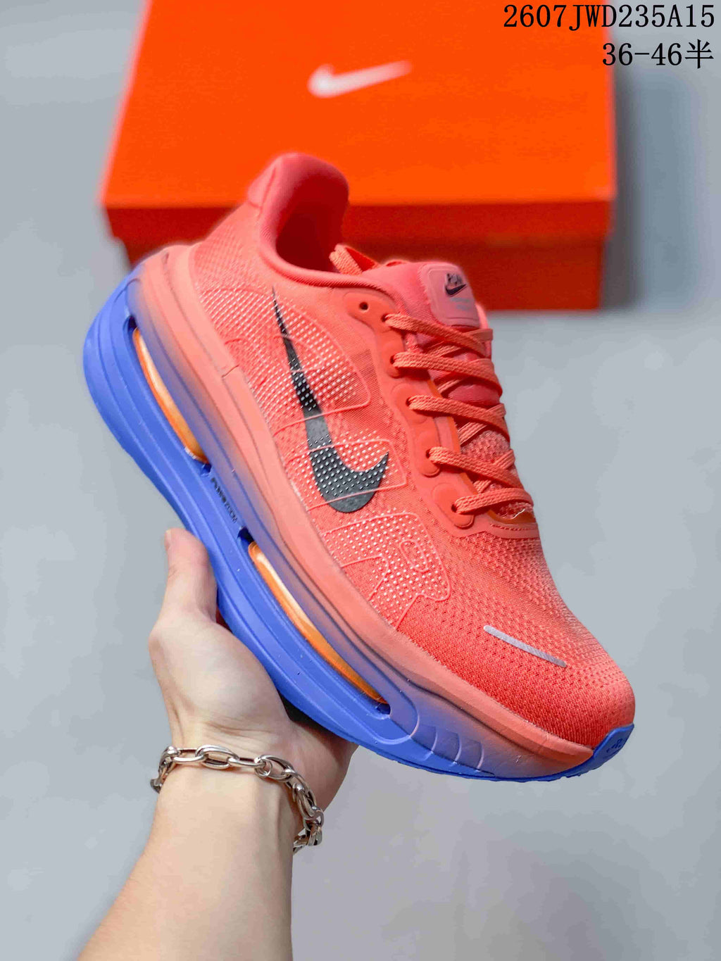 Angled side view of a coral Nike Vomero Premium running shoe with black Swoosh and blue-orange sole.