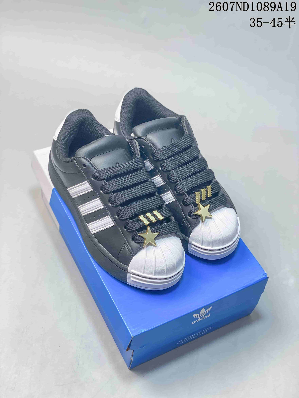 Black-and-white adidas Superstar-style shell-toe sneakers displayed on a blue shoebox.
