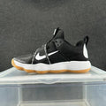 Side view of black Nike sneakers with a white Swoosh, wraparound printed strap, white midsole, and gum-colored outsole.