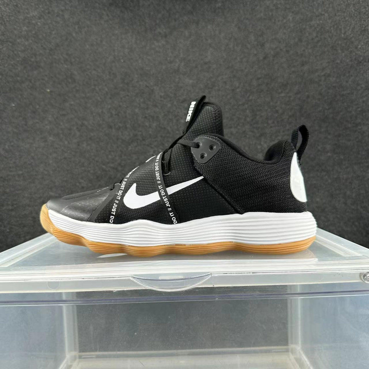 Side view of black Nike sneakers with a white Swoosh, wraparound printed strap, white midsole, and gum-colored outsole.