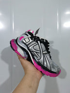 Close-up angled view of silver, black, and fluorescent pink Balenciaga Runner sneakers held against a light background.