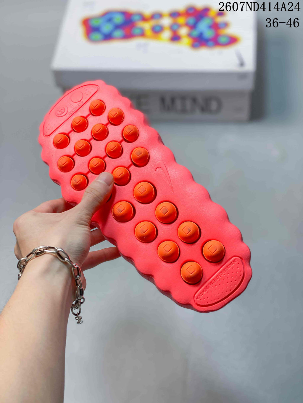 Bottom view of a coral-red Nike Mind 001 mule showing its raised circular outsole elements and textured tread.