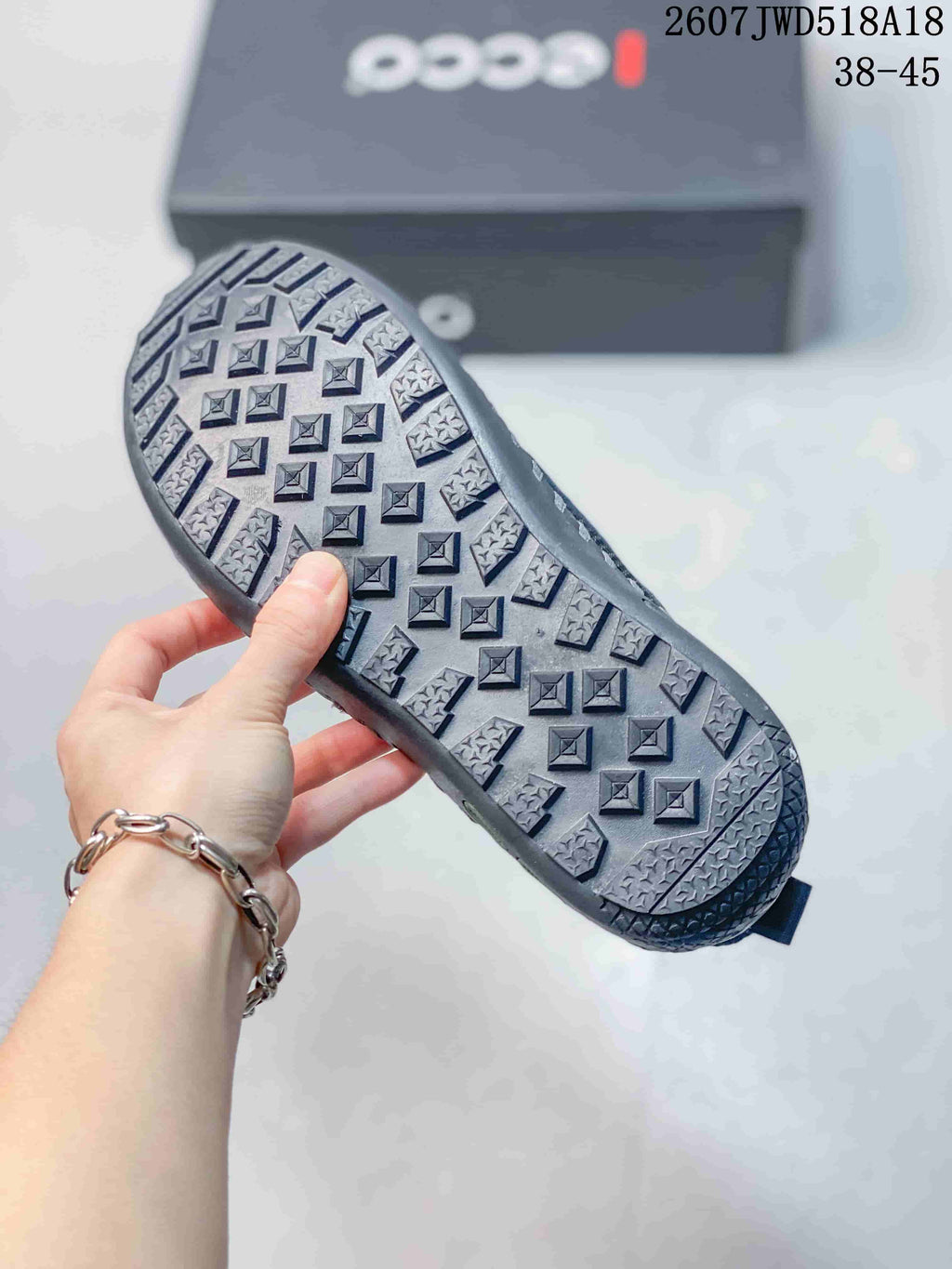 Underside view of a black sneaker showing the patterned rubber outsole and ECCO shoebox in the background.