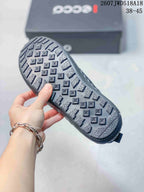 Underside view of a black sneaker showing the patterned rubber outsole and ECCO shoebox in the background.