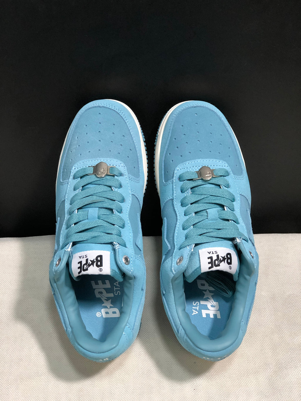 Top-down view of the pair showing light blue laces, perforated toe boxes, metallic lace accessories, and branded insoles.