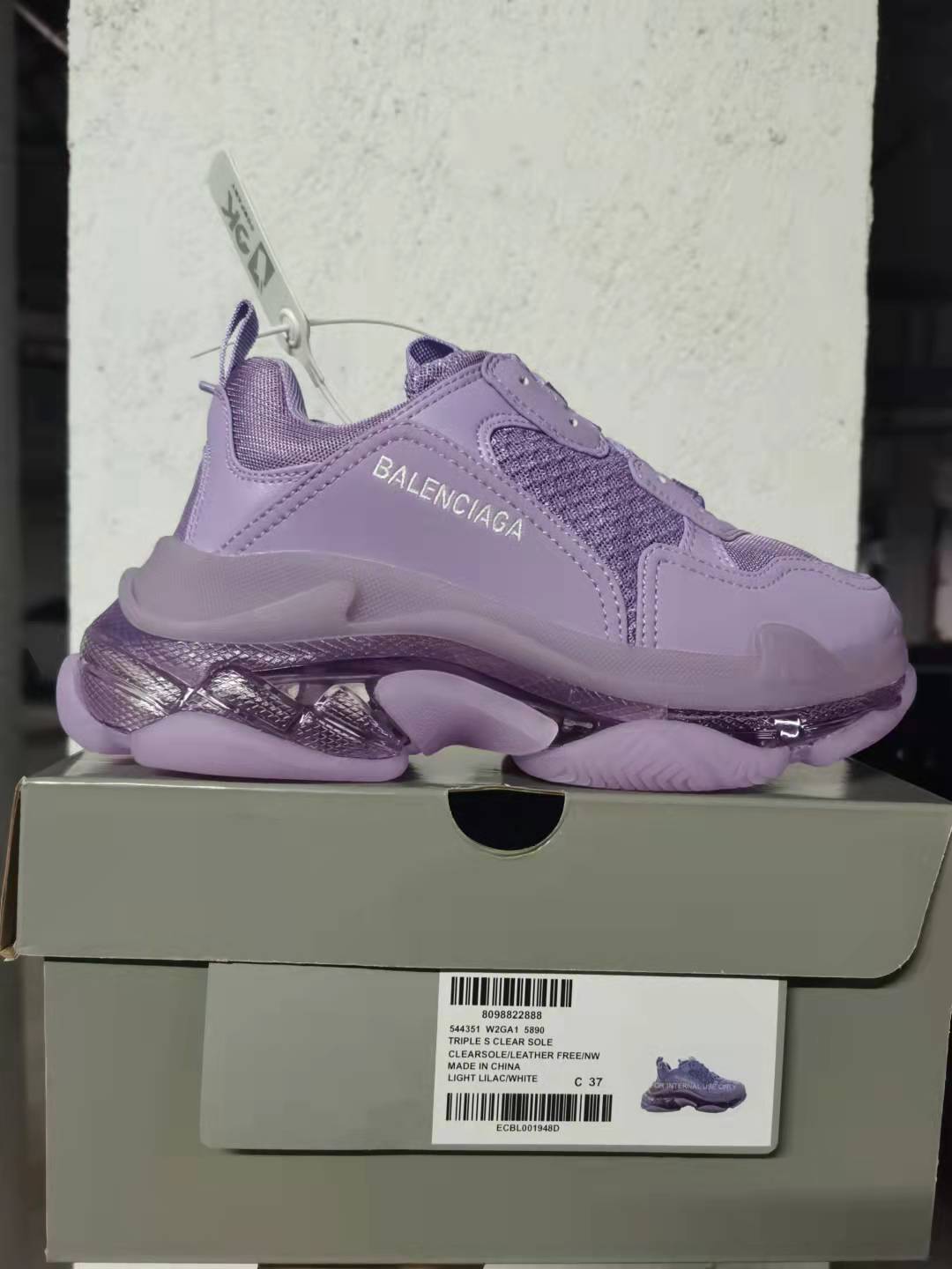 Purple Balenciaga Triple S sneaker shown on its box, with side branding and a box label visible.