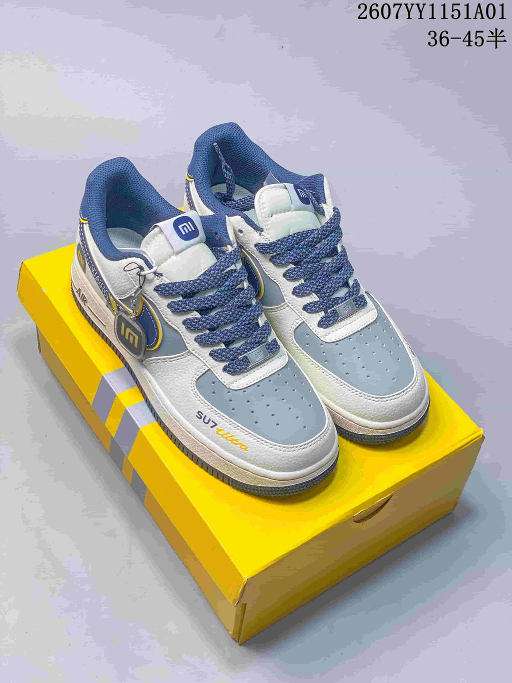 Nike Air Force 1 ’07 Low sneakers with white, blue-gray, and yellow details on a yellow box.
