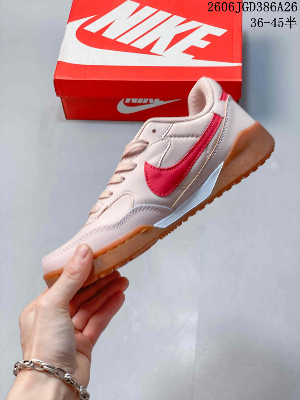 Side view of the pale pink sneaker with red Nike side branding, layered panels and a gum-colored outsole.