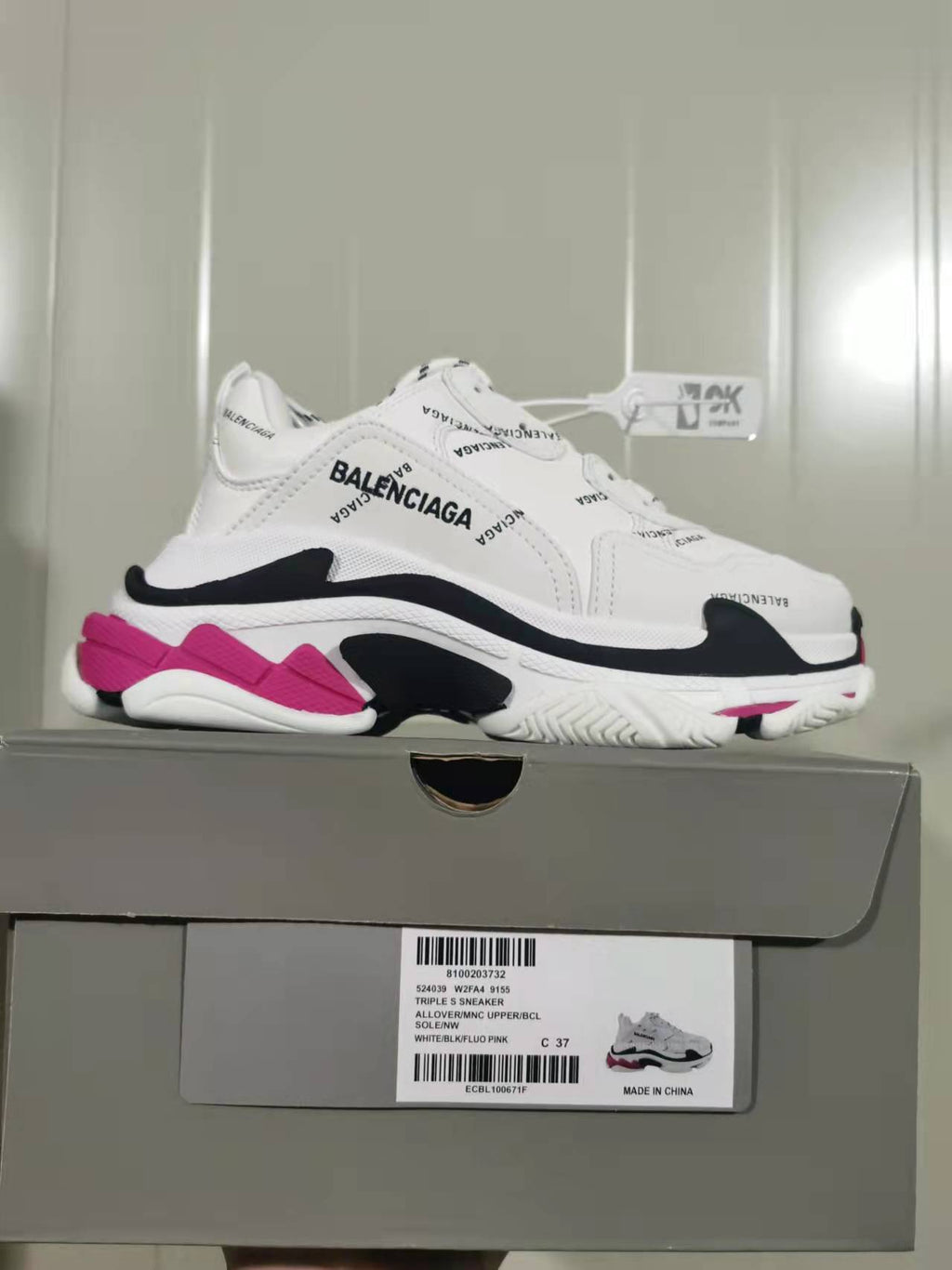 White Balenciaga Triple S sneaker with black and pink accents displayed on its shoe box; the box label shows style code 9155 and size C 37.