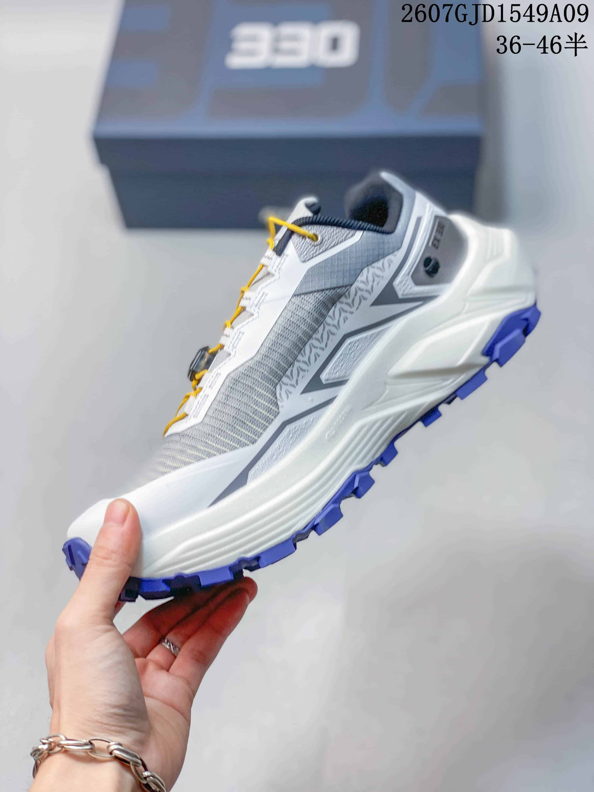 Side profile showing the grey textile-style upper, layered white midsole, heel structure, and purple outsole.