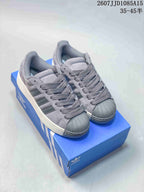 Pair of grey Adidas Superstar XLG sneakers displayed on a blue shoebox, showing the shell toes, laces, side stripes, and thick soles.