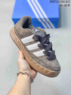 Angled side view of the Adidas Adimatic Low sneaker showing the brown upper, white stripes, dark laces, and gum outsole.