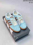 Pair of light blue adidas VL Court Classic sneakers with brown stripes, cream laces, and gum-colored soles on a shoebox.