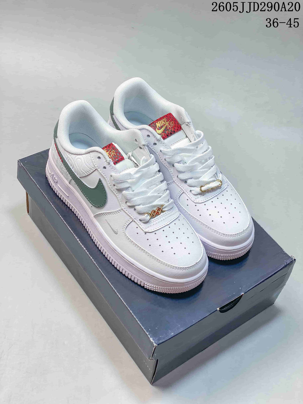 Pair of white Nike Air Force 1 sneakers with green and red accents displayed on a shoebox; overlay shows style code JD290A20 and size range 36-45.