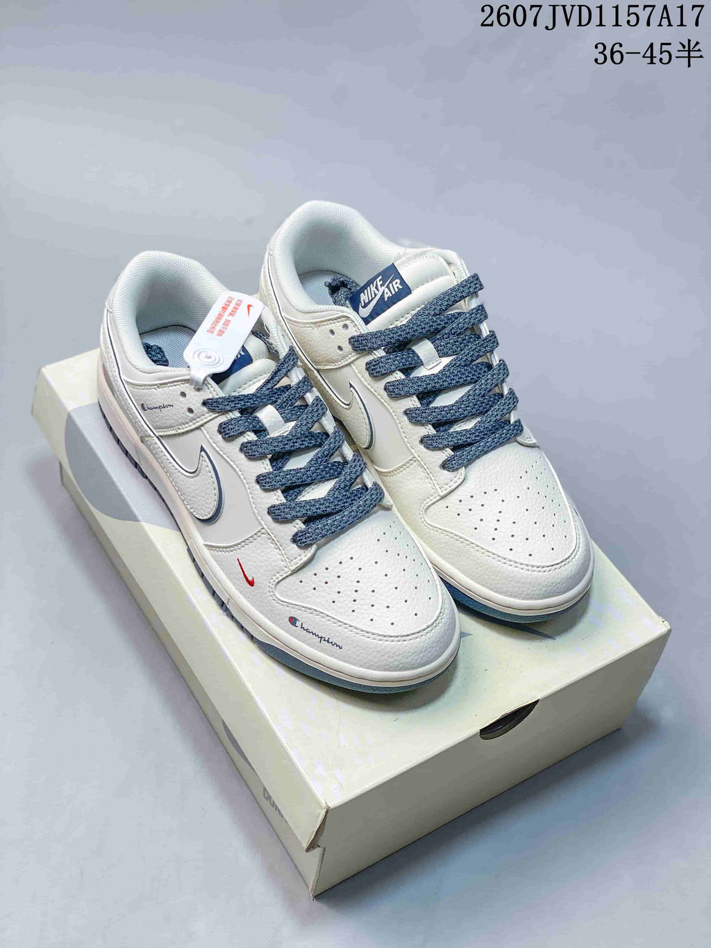 Pair of white and blue low-top sneakers displayed on a shoebox, with blue laces and style code 2607JVD1157A17 visible above.