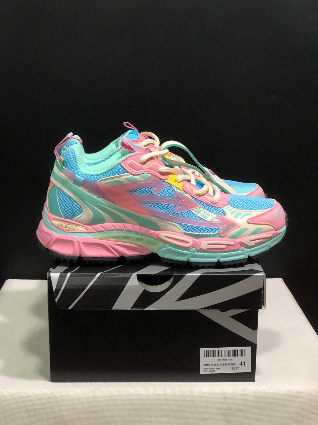 Side view of the colorful pink, mint and blue sneakers resting on a black-and-white branded shoe box.